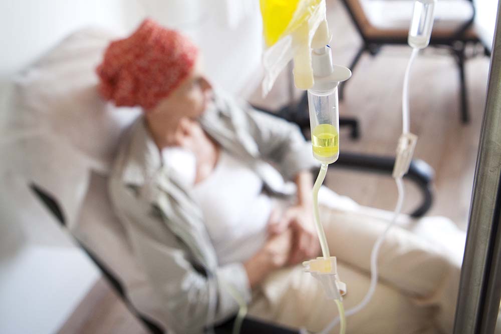 Vrouw met oranje hoofddoek zit op stoel en heeft een chemotherapie-infuus