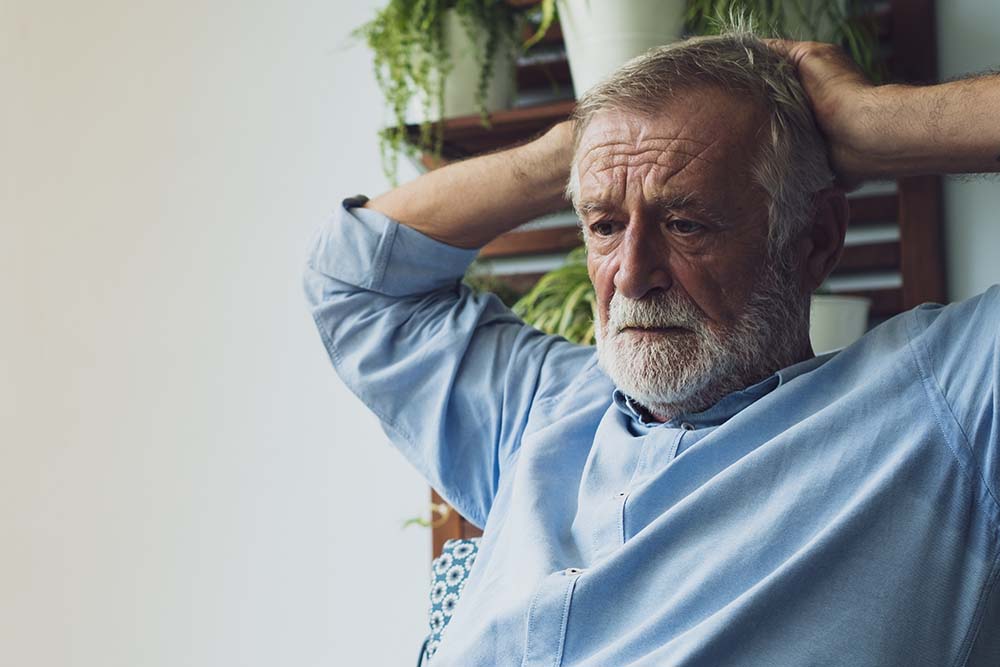 oudere man met baard, vanaf zijn middel in beeld, staart naar links buiten beeld met de handen achter het hoofd gevouwen