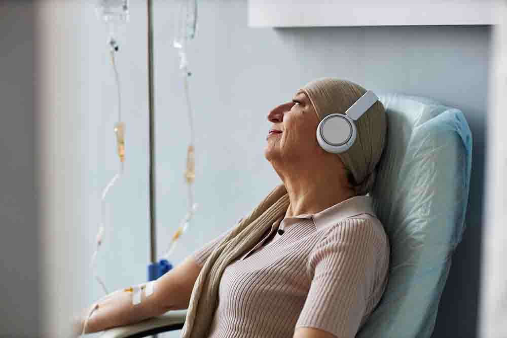 Een vrouw met hoofdbedekking ligt in een stoel met een koptelefoon op terwijl ze chemokuur krijgt