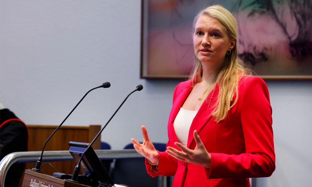 Eline, een witte vrouw met blond haar, presenteert achter een katheder in de aula van de Radboud Universiteit