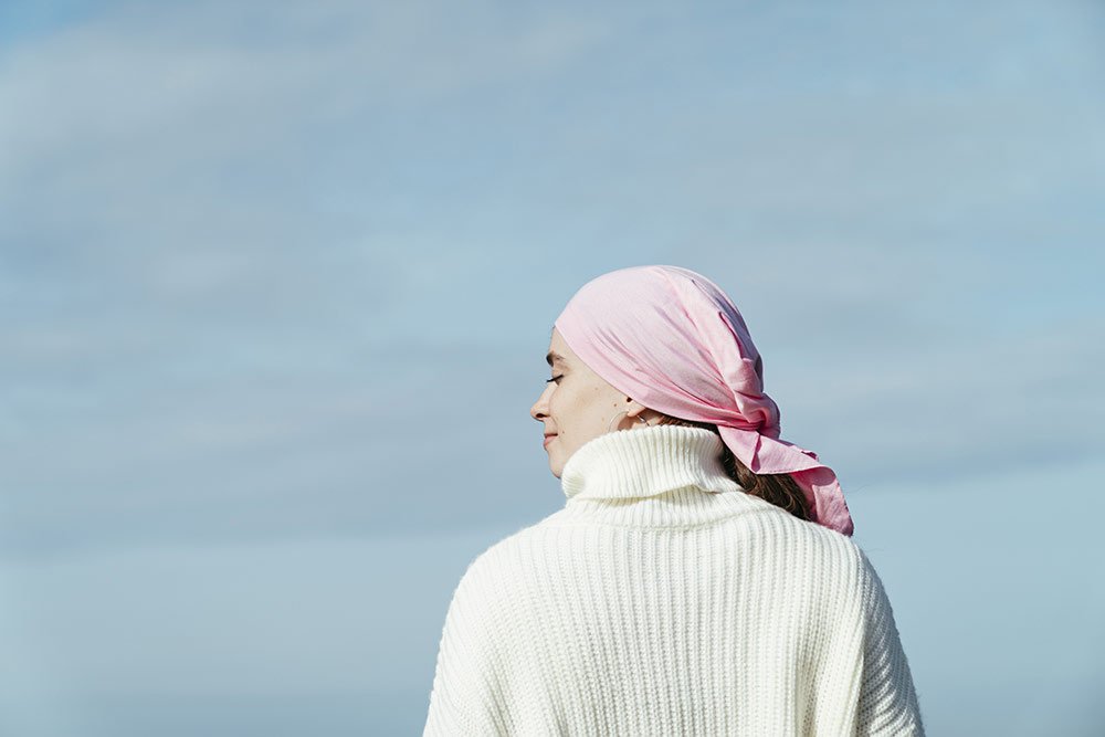 vrouw met witte trui en roze hoofddoek tegen achtergrond van blauwe lucht