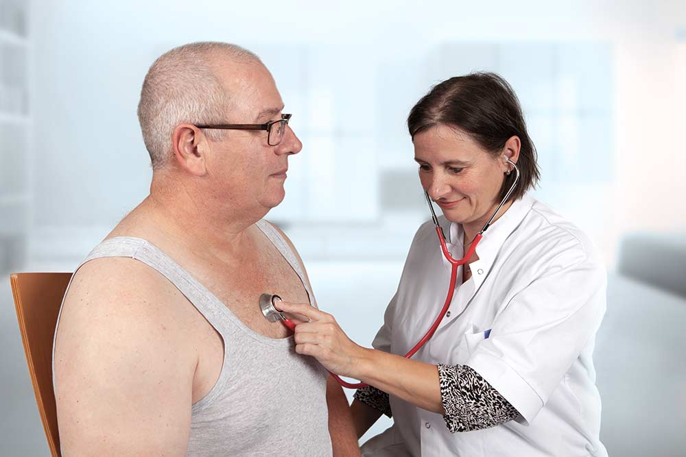 Vrouwelijke arts luistert naar longen bij oudere man