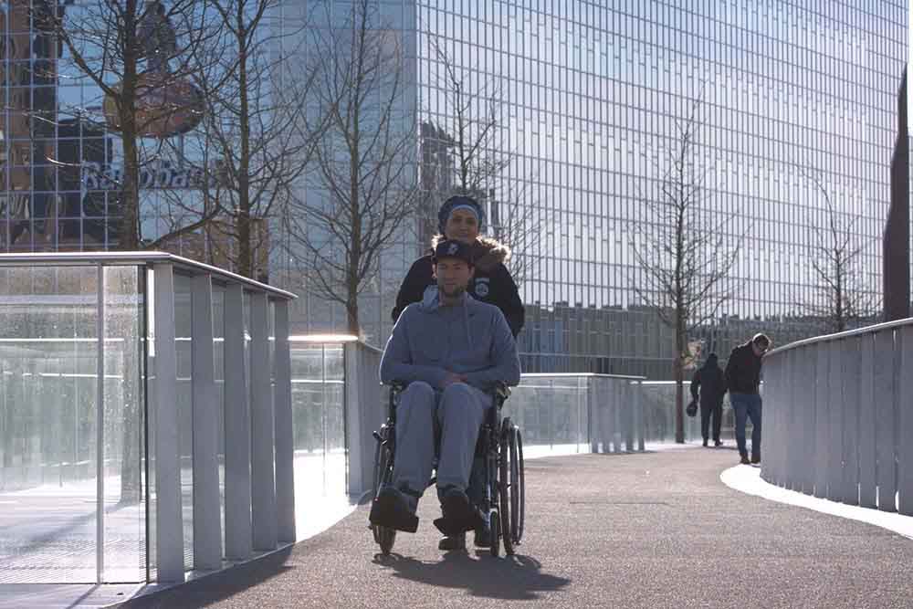 vrouw duwt man in rolstoel over brug